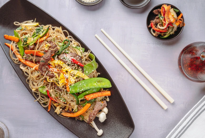 a close up of a plate of food with chopsticks, 🦩🪐🐞👩🏻🦳, on grey background, noodles, red meat shreds