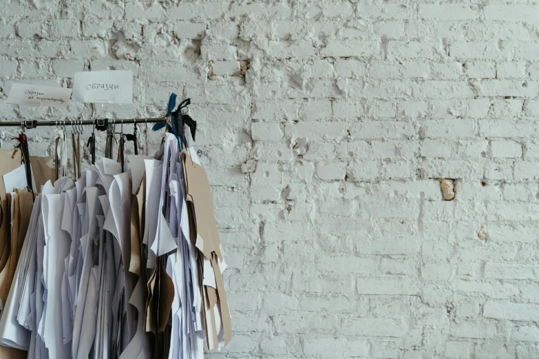 clothes hanging on a rack in front of a brick wall, pexels contest winner, made of paper, storefront, off - white collection, thumbnail