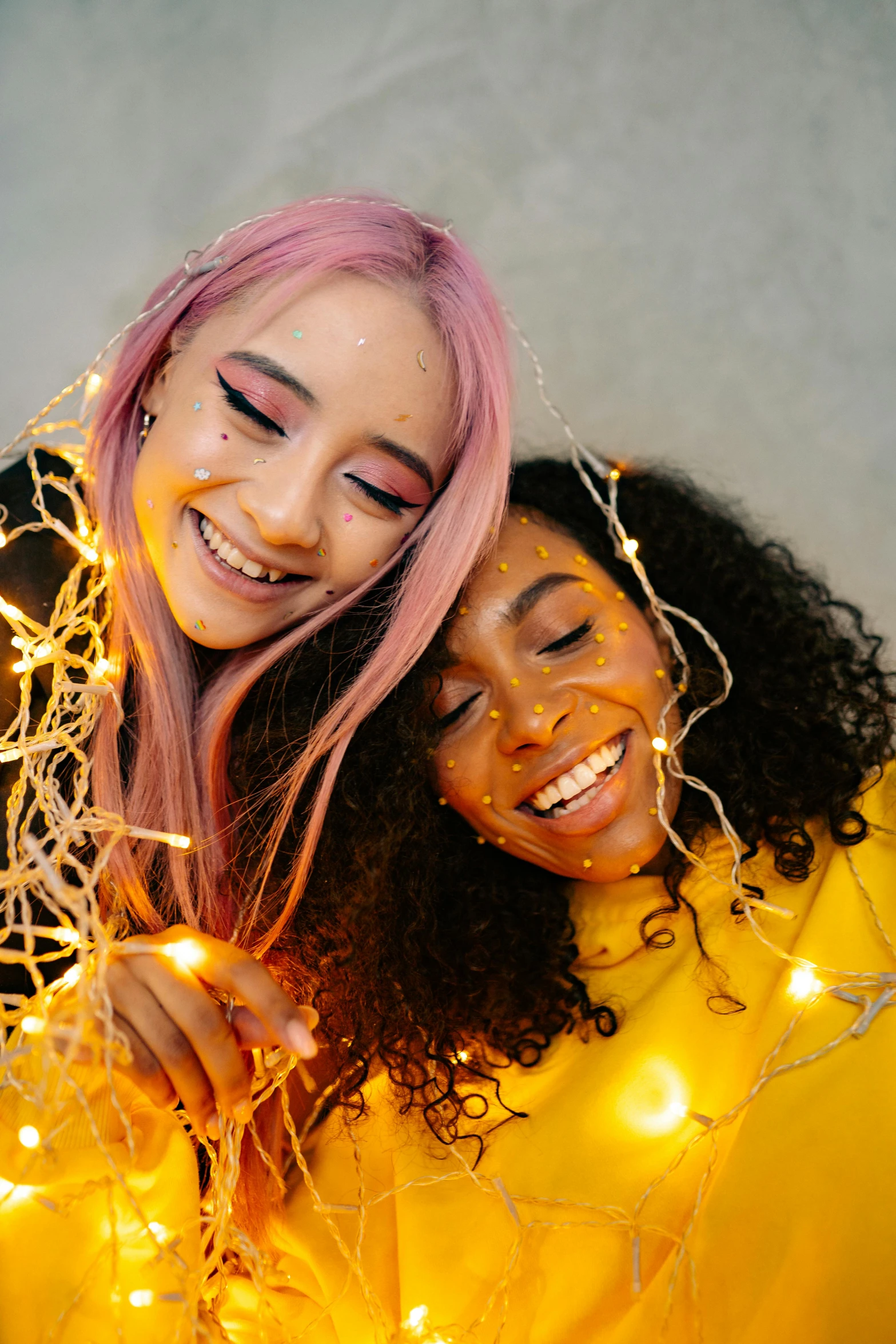 a couple of women standing next to each other, trending on pexels, long glowing colourful hair, fairy lights, happy friend, diverse