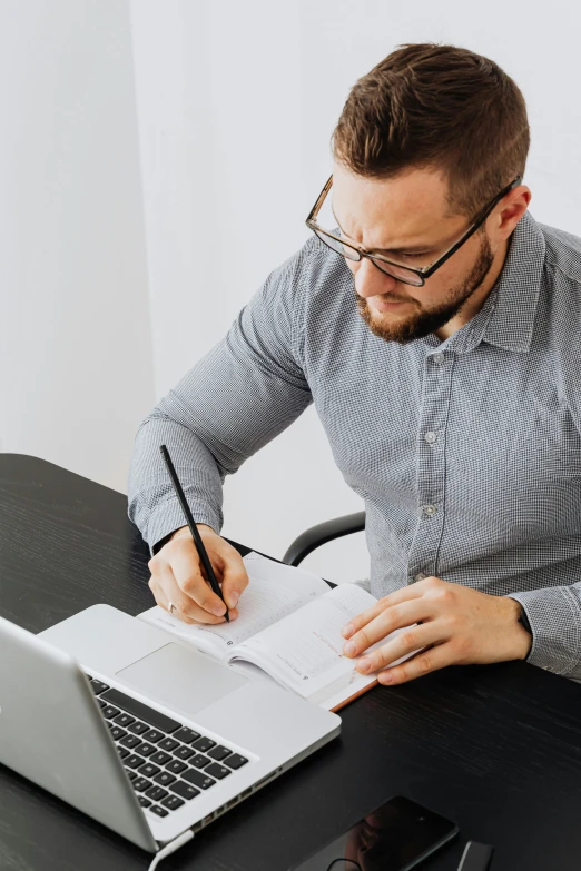 a man sitting at a desk writing on a piece of paper, it specialist, holding notebook, thumbnail, upper body image