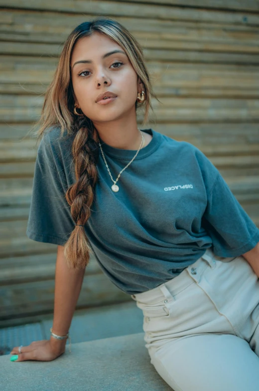 a woman sitting on a ledge wearing a blue shirt and white pants, a portrait, by Robbie Trevino, trending on pexels, in tshirt, portrait sophie mudd, promotional image, neck zoomed in