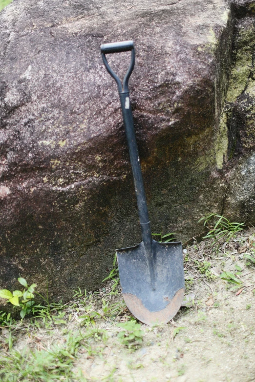 shovel sitting on the ground next to a rock