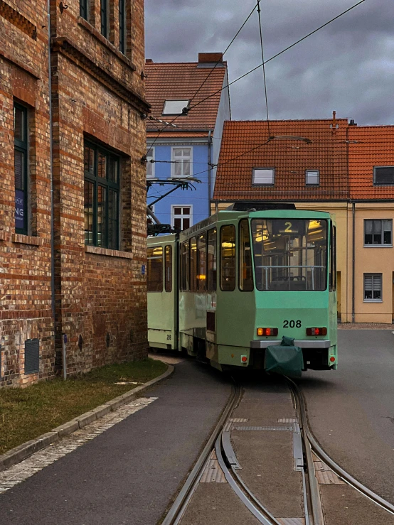 a green trolley traveling down a street next to a brick building, inspired by Christian Krohg, pexels contest winner, panorama, grey, street tram, color image