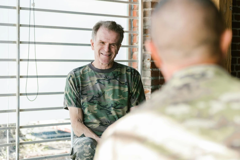 a man in camouflage sitting in front of a window, a portrait, unsplash, smug smile, randy travis, avatar image, wearing military uniform