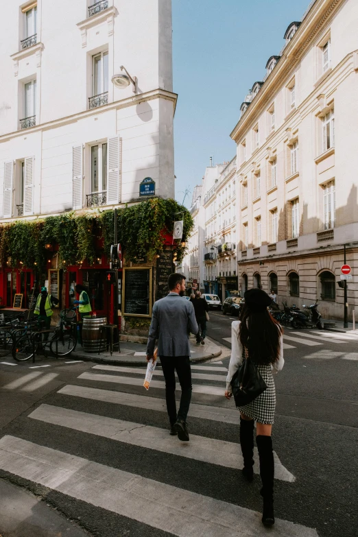 a couple of people walking across a street, trending on unsplash, paris school, lush surroundings, exterior, merchants, ground level shot