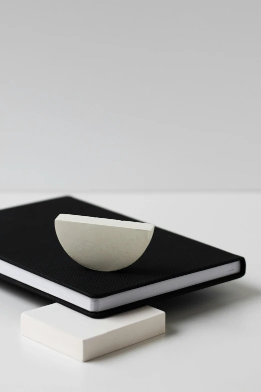 a white bowl sitting on top of a black book, an abstract sculpture, inspired by jeonseok lee, trending on unsplash, notebook, square nose, half moon, silver，ivory