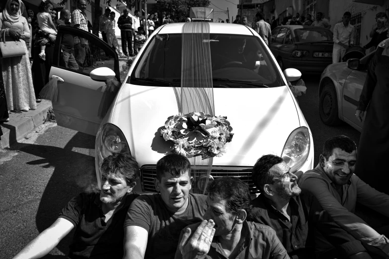 a group of people sitting in front of a car, a black and white photo, by Giovanni Pelliccioli, funeral veil, greek nose, flower power, celtic