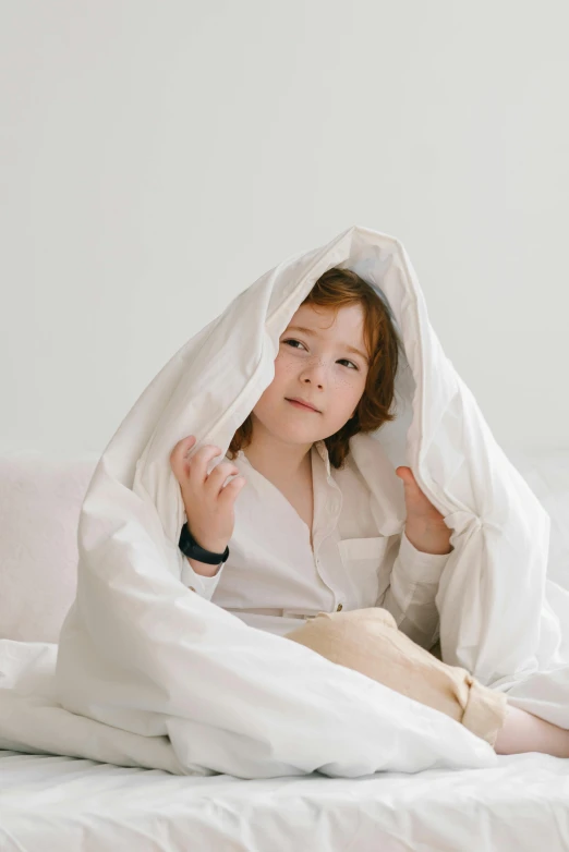 a little girl sitting on top of a bed under a blanket, wearing a white shirt, boy with neutral face, thumbnail, product shot