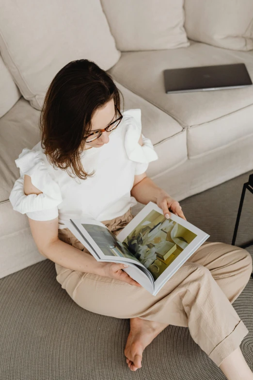 a woman sitting on the floor reading a book, a picture, pexels contest winner, wearing a white button up shirt, at the sitting couch, product introduction photo, wearing elegant casual clothes