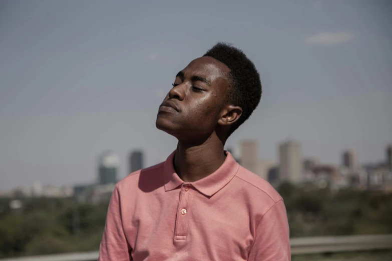 a man standing in front of a city skyline, by Afewerk Tekle, pexels contest winner, boy with neutral face, eyes closed, looking upwards, rosen zulu