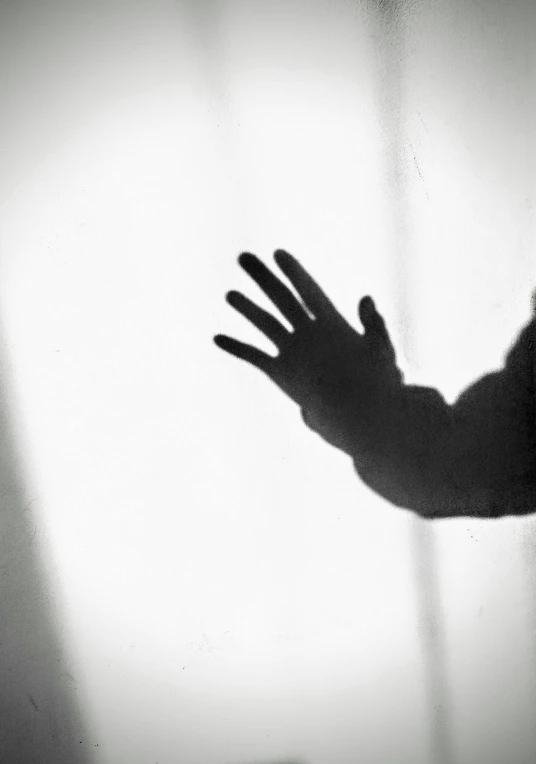 a silhouette of a person holding their hand up, a black and white photo, by John Hutton, shadowcreature, istock, glass, concerned