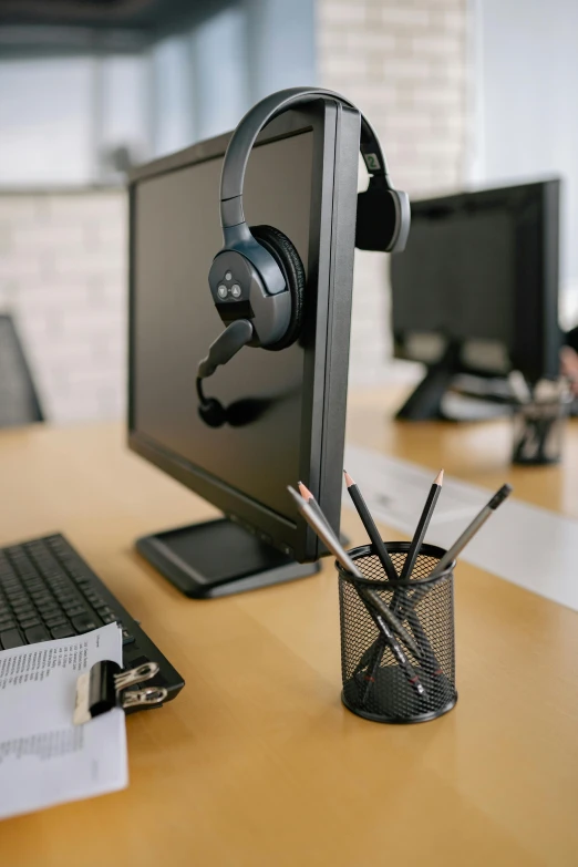 a desktop computer sitting on top of a wooden desk, with head phones, pencils, curated collections, bronze headset