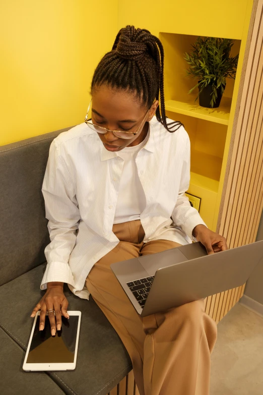 a woman sitting on a couch using a laptop, trending on pexels, happening, wearing lab coat and a blouse, yellow carpeted, afro tech, thumbnail