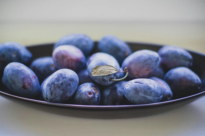 a bowl filled with blue plums on top of a table, unsplash, ((purple)), plates of fruit, shallow depth of focus, illustration »