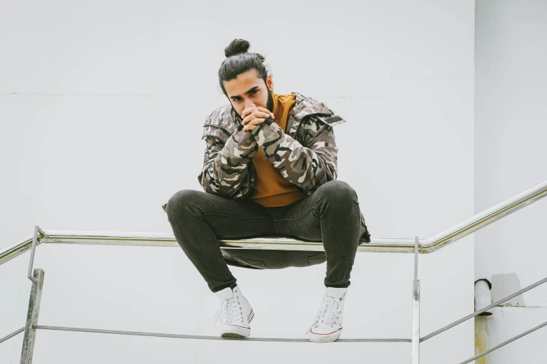 a man sitting on a railing talking on a cell phone, inspired by Pablo Rey, trending on pexels, realism, singer maluma, battle pose, thinking pose, wearing camo