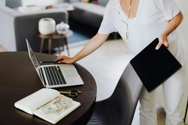 a woman standing in front of a laptop computer, by Arabella Rankin, pexels contest winner, cash on a sidetable, business surrounding, from waist up, papers on table