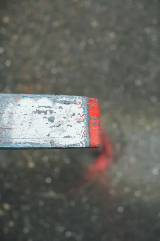 a close up of a metal object on the ground, half red, head straight down, colour corrected, scratched