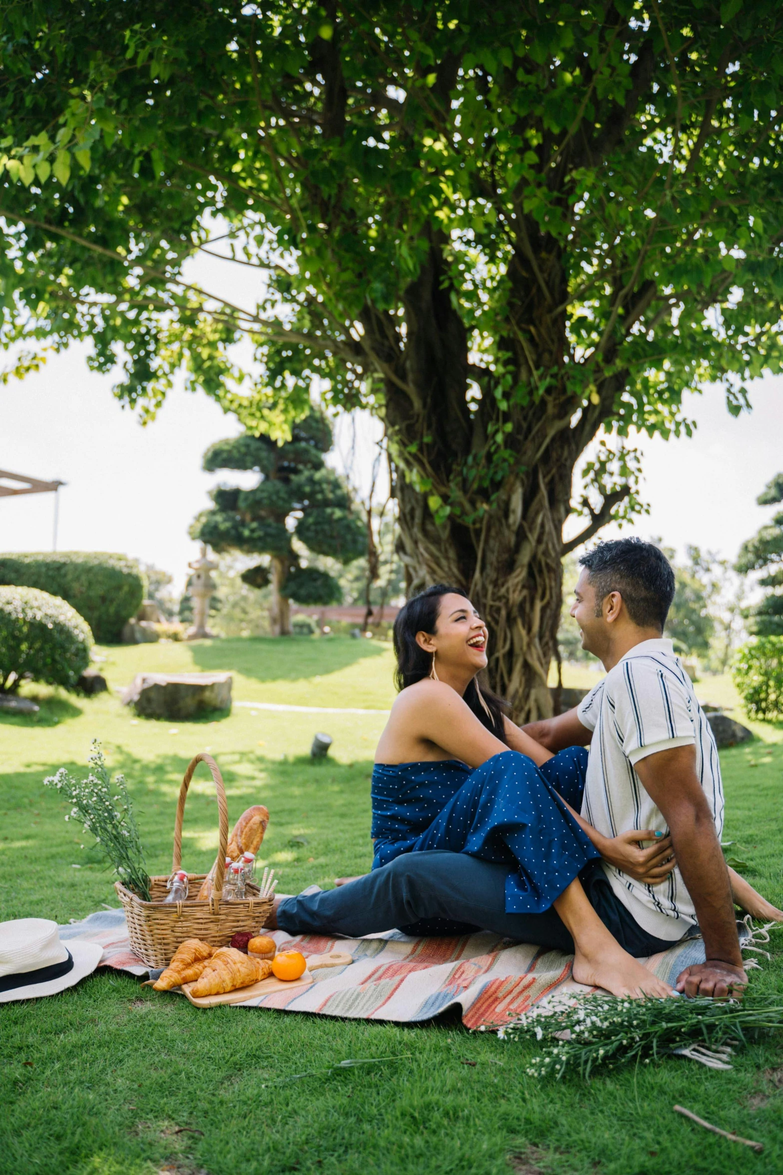 a man and woman sitting on a blanket under a tree, lush garden surroundings, breakfast, hoang lap, playful