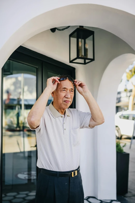 man stands outside building adjusting his hair with both hands