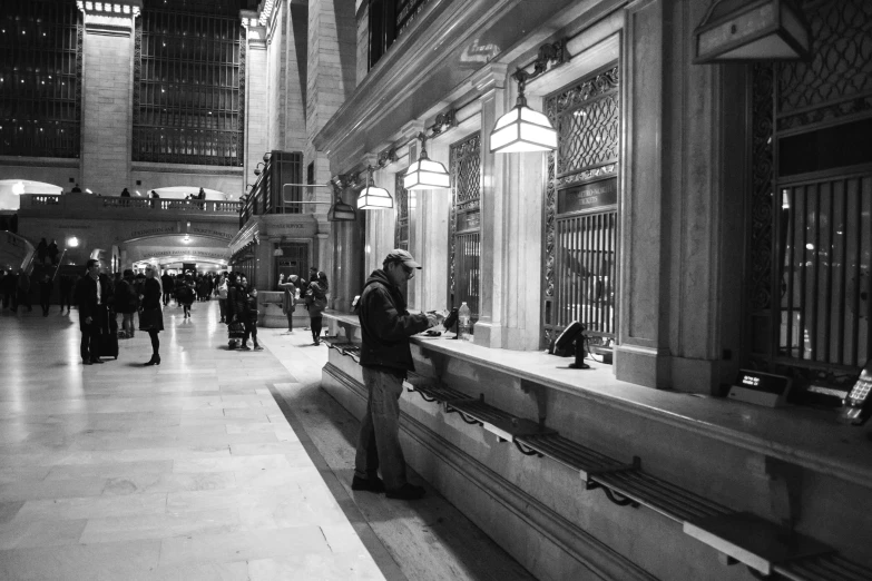 a black and white photo of people in a train station, inspired by Thomas Struth, pexels, art nouveau, on a marble pedestal, looking at his phone, tending on art station, new york