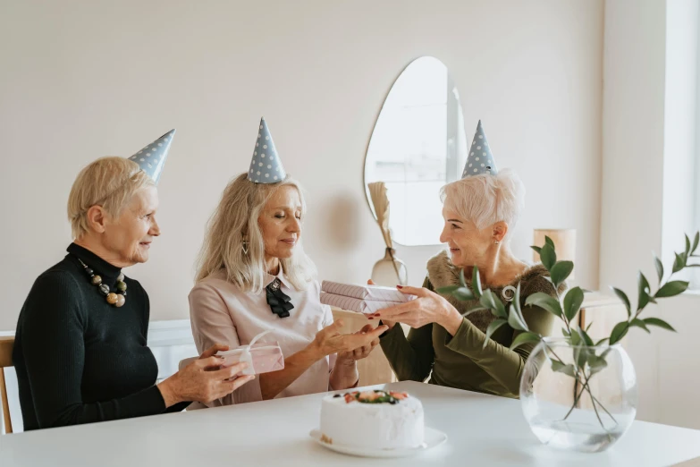 three women sitting at a table with a birthday cake, by Emma Andijewska, pexels contest winner, white haired lady, party hats, background image