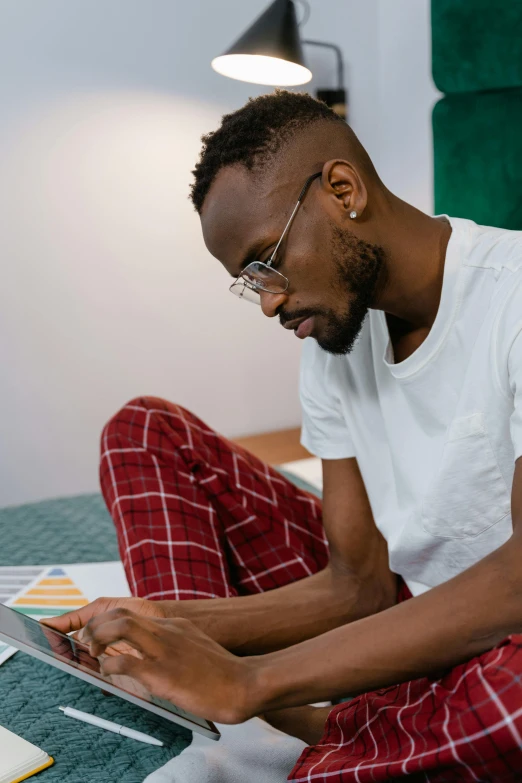 a man sitting on a bed using a laptop computer, a photo, trending on pexels, afrofuturism, white reading glasses, multicoloured, student, no watermarks