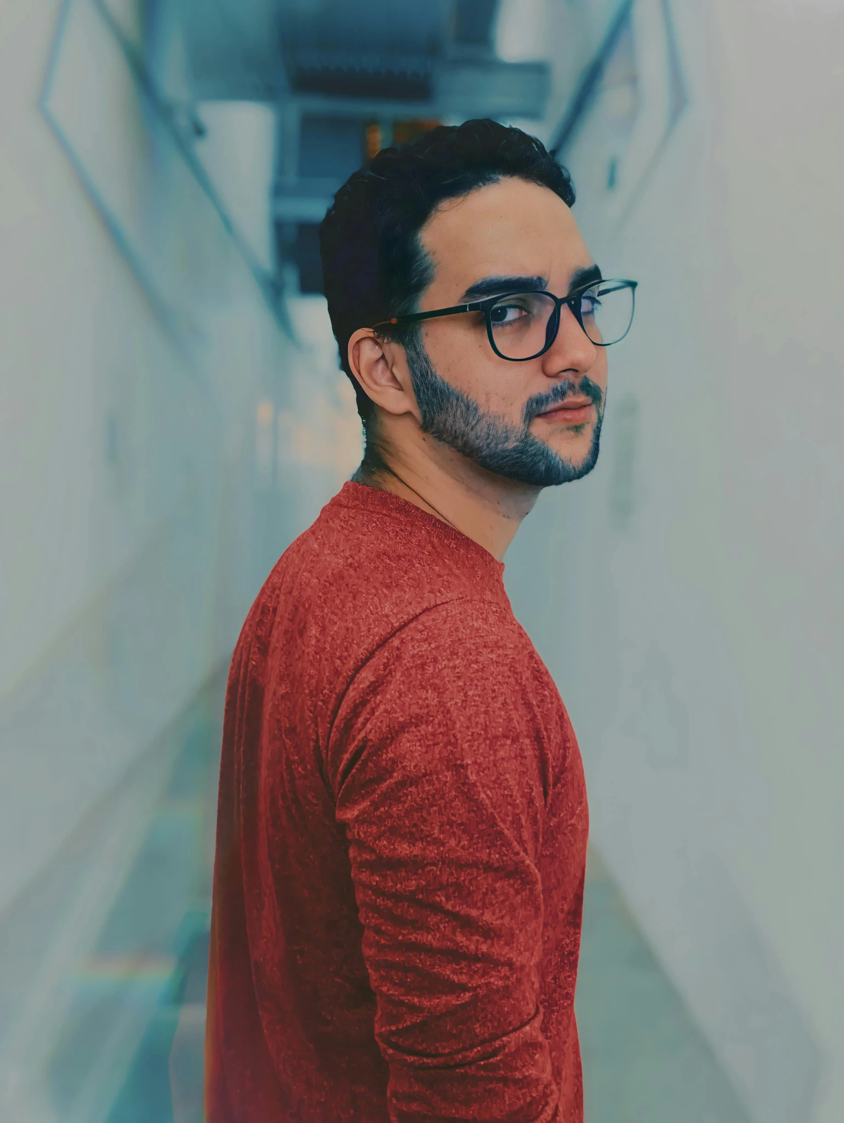 a man with glasses standing in a hallway, an album cover, inspired by Ismail Acar, pexels contest winner, light stubble with red shirt, gif, profile pic, lgbtq