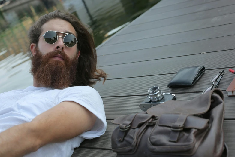 a man with a beard laying on a dock, trending on reddit, the handbag is over a wood table, aboriginal australian hipster, avatar image, mid long hair