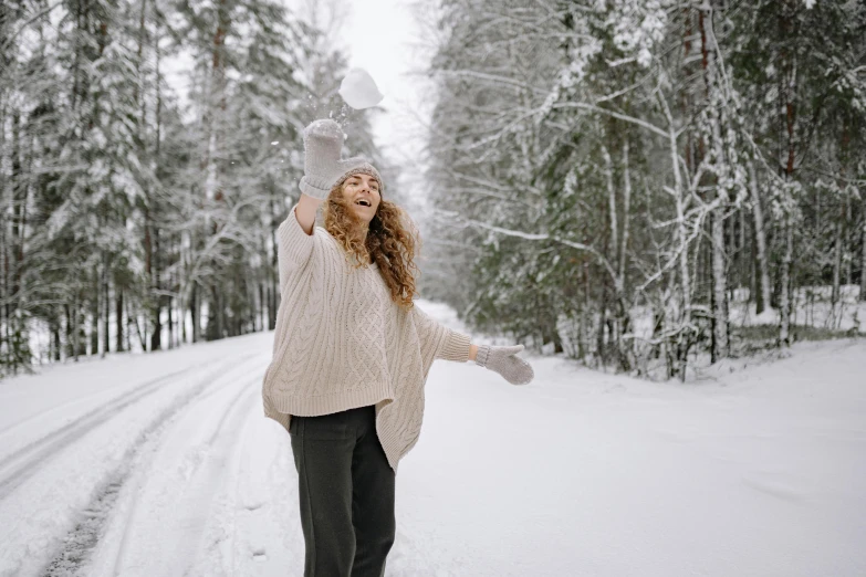 woman in tan sweater tossing snow into air over snow covered road