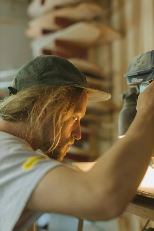 a man in a hat working on a machine, an airbrush painting, unsplash contest winner, blonde man, indie film, ignant, carpenter