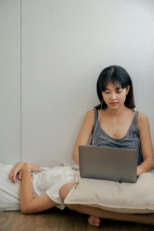 a woman sitting on the floor using a laptop, by helen huang, trending on pexels, happening, couple on bed, on a gray background, chinese woman, connectivity