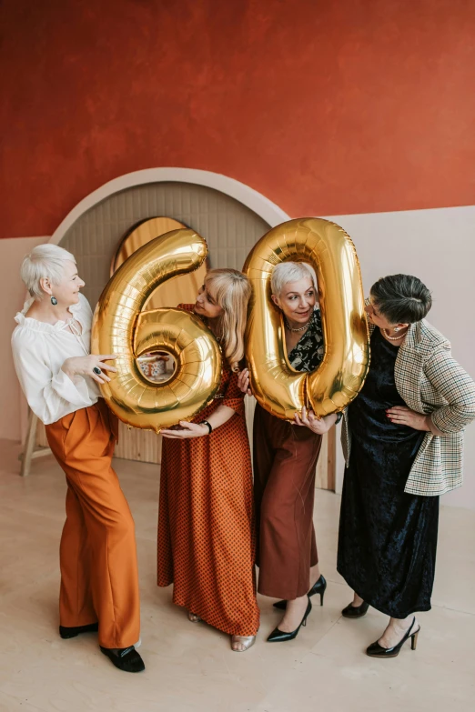 a group of women standing next to each other holding gold balloons, a polaroid photo, by Julia Pishtar, pexels contest winner, he is about 6 0 years old, brown clothes, wrinkles, celebrating a birthday