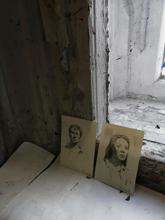 a couple of pictures sitting on top of a window sill, a charcoal drawing, photo of poor condition, inside the building, ((portrait)), art sketches