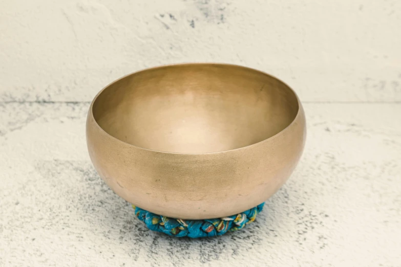 a metal bowl sitting on top of a table, an album cover, by Elaine Hamilton, unsplash, cloisonnism, brass equipment and computers, teal cloth, meditation, beige