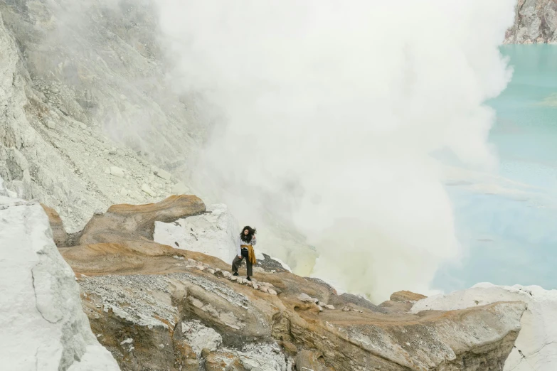 a man is standing on a hill overlooking a geyser