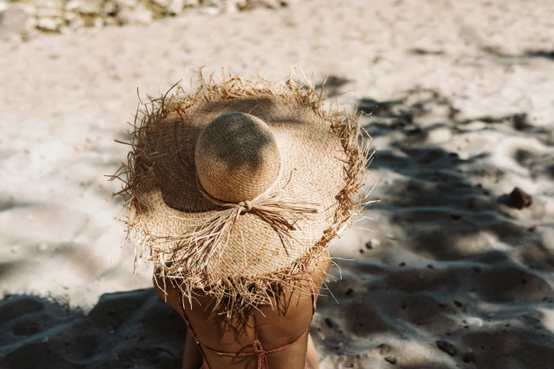a woman sitting in the sand wearing a straw hat, by Anna Boch, pexels contest winner, close-up shot from behind, with a halo of unkempt hair, manly, sunny day time