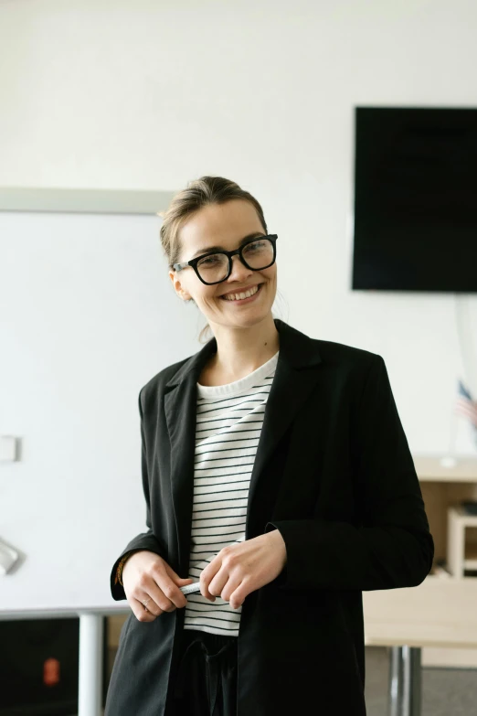 a woman standing in front of a white board, wearing a suit and glasses, looking happy, standing in class, it specialist