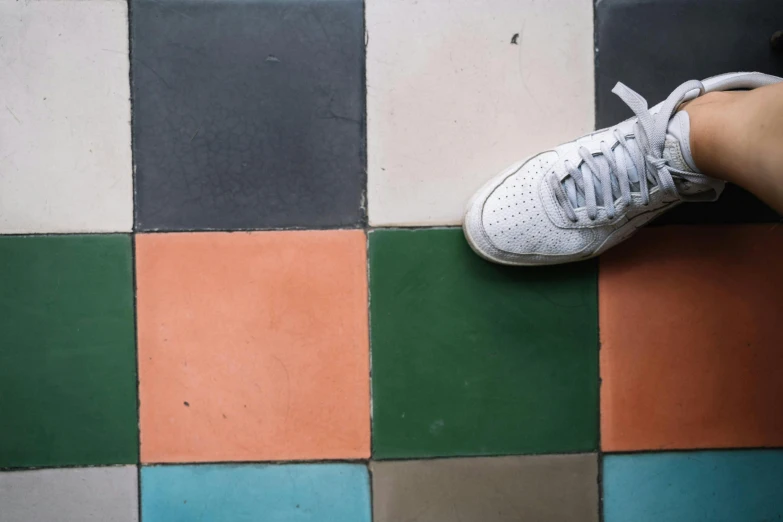 a close up of a person's shoes on a tiled floor, inspired by Wes Anderson, trending on unsplash, color field, multicoloured, muted green, dark grey and orange colours, with a square