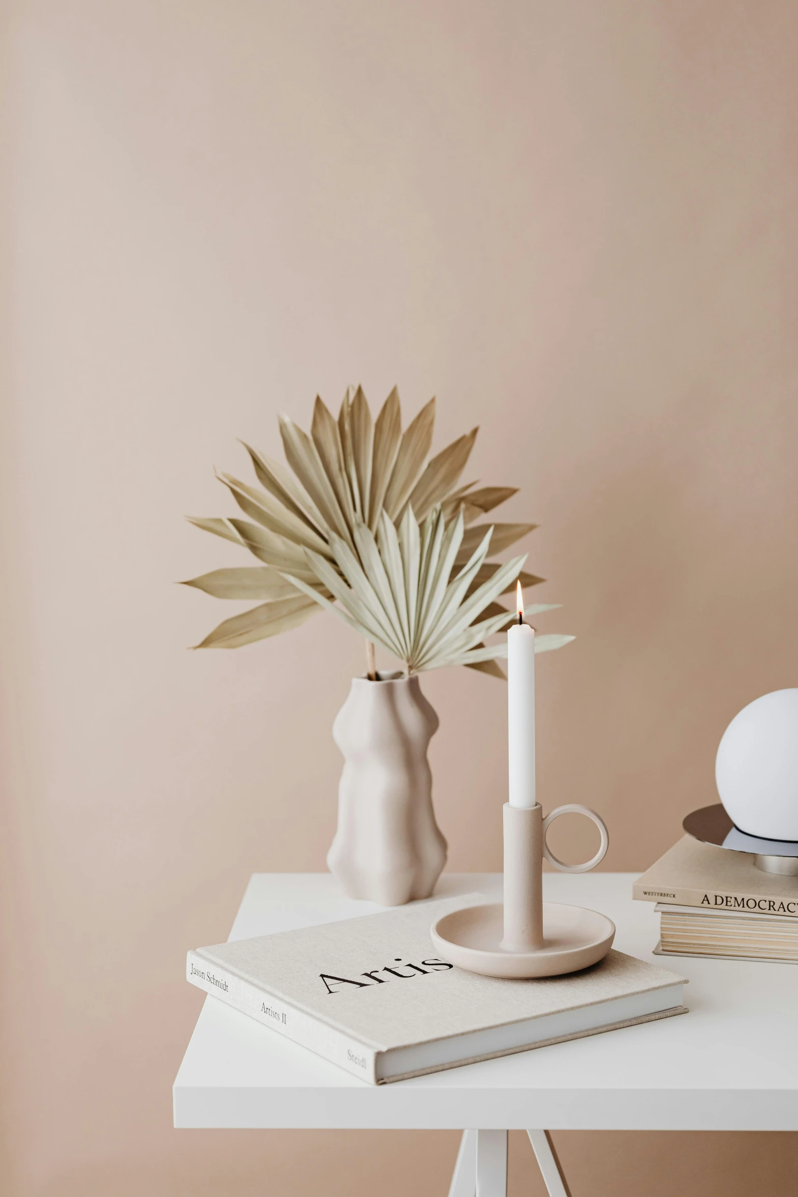 a white table topped with a vase filled with flowers, an abstract sculpture, inspired by Giorgio Morandi, featured on pinterest, minimalism, holding a candle holder, palm, sand color, soft blush