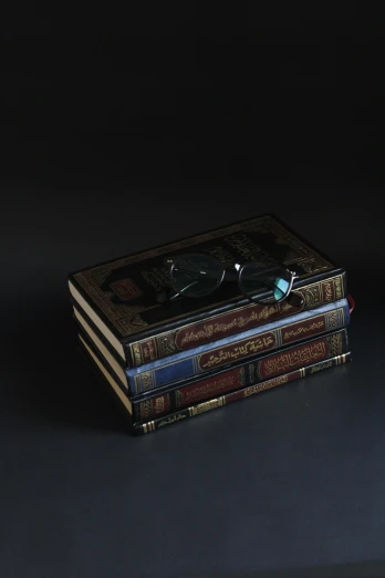 a stack of books sitting on top of a table, inspired by Osman Hamdi Bey, featured on reddit, hyperrealism, black lacquer, floating cars, high angle shot, jewelry engraved in scarab
