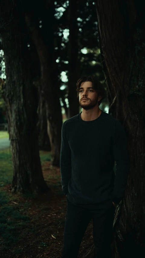 man in a dark forest wearing a black sweater