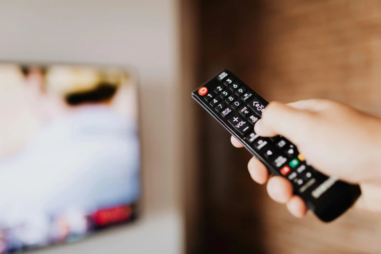 a person holding a remote control in front of a television, by Carey Morris, pexels, 🦩🪐🐞👩🏻🦳, avatar image, news footage, gold