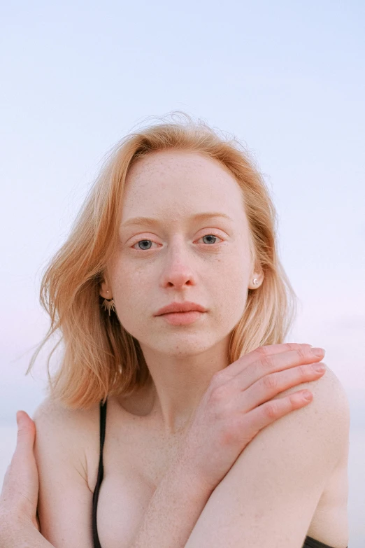 a woman sitting on top of a beach next to the ocean, an album cover, trending on pexels, renaissance, pale round face, miranda otto, soft portrait shot 8 k, albino skin