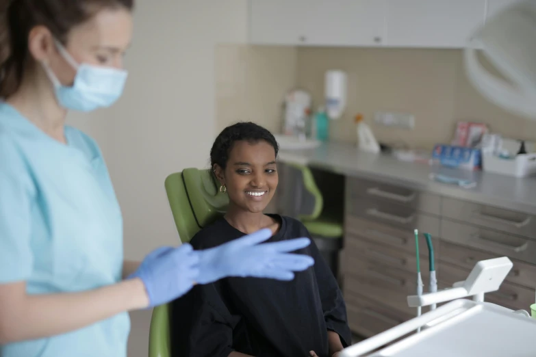a woman sitting in a chair in front of a dentist, pexels contest winner, hurufiyya, ( ( dark skin ) ), large black smile, clean medical environment, avatar image