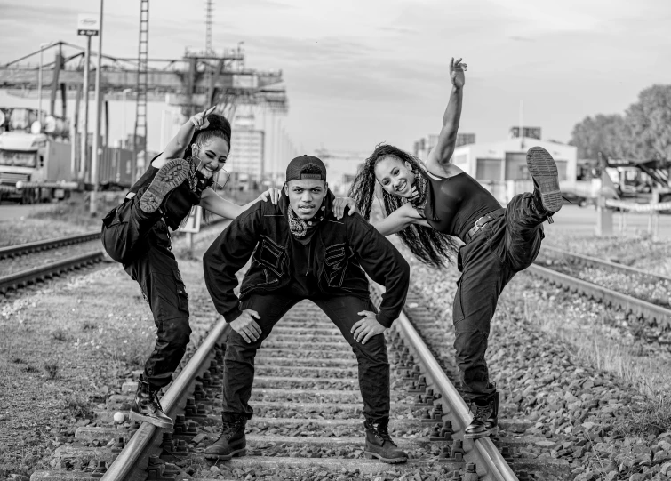 three men with jeans and jackets stand on the railroad tracks