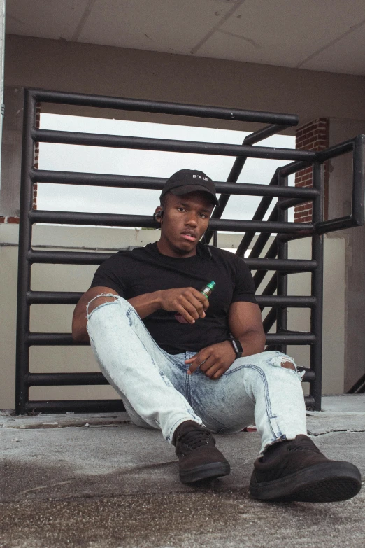 a man sitting on the ground smoking a cigarette, an album cover, inspired by Terrell James, trending on pexels, realism, he is wearing a black t-shirt, ( ( dark skin ) ), at college, hero pose