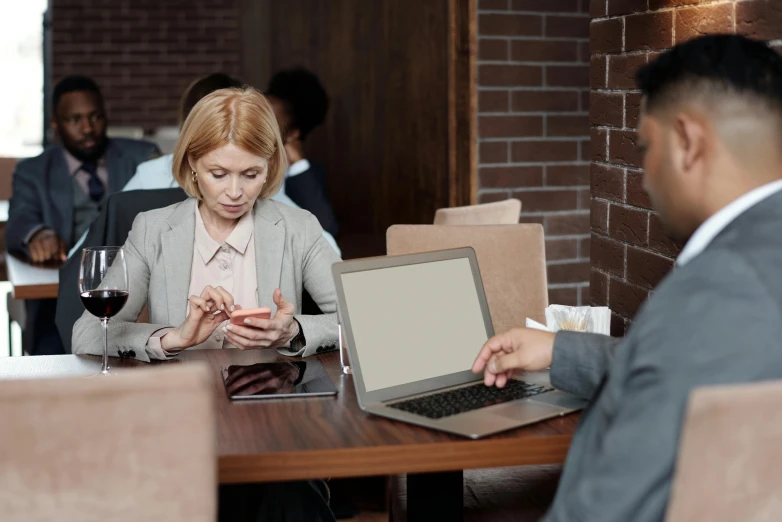 a man and a woman sitting at a table with a laptop, trending on pexels, woman in business suit, brown, she is holding a smartphone, a blond