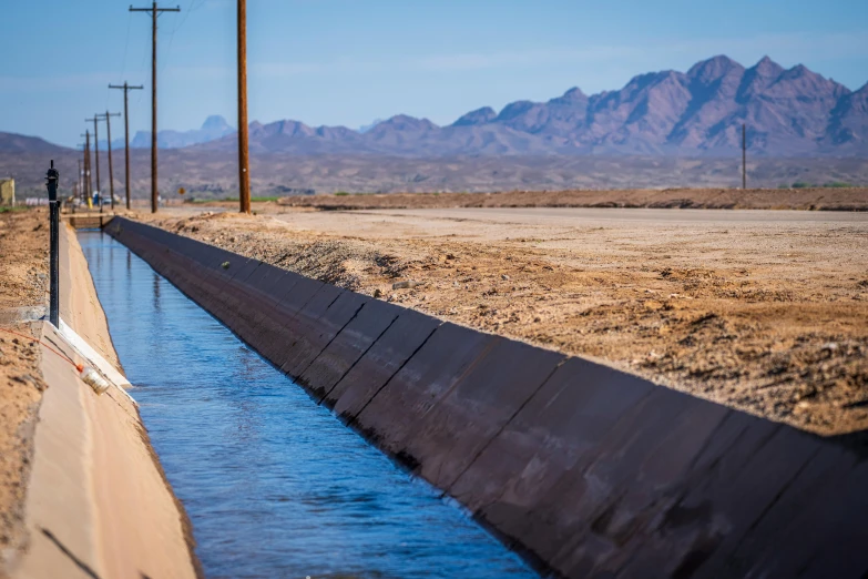 a drain in the middle of a desert with mountains in the background, water running down the walls, infrastructure, lynn skordal, profile image