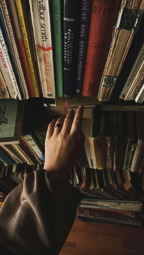 a person reaching for a book on a bookshelf, an album cover, trending on pexels, high angle shot, vintage aesthetic, high quality photo, studious