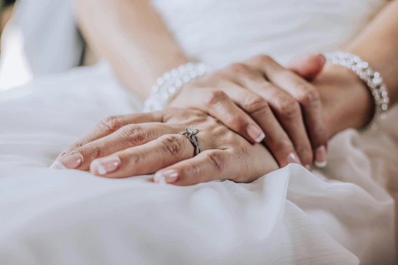 a close up of a person holding a wedding ring, unsplash, sitting on a bed, woman holding another woman, silver，ivory, colour photograph